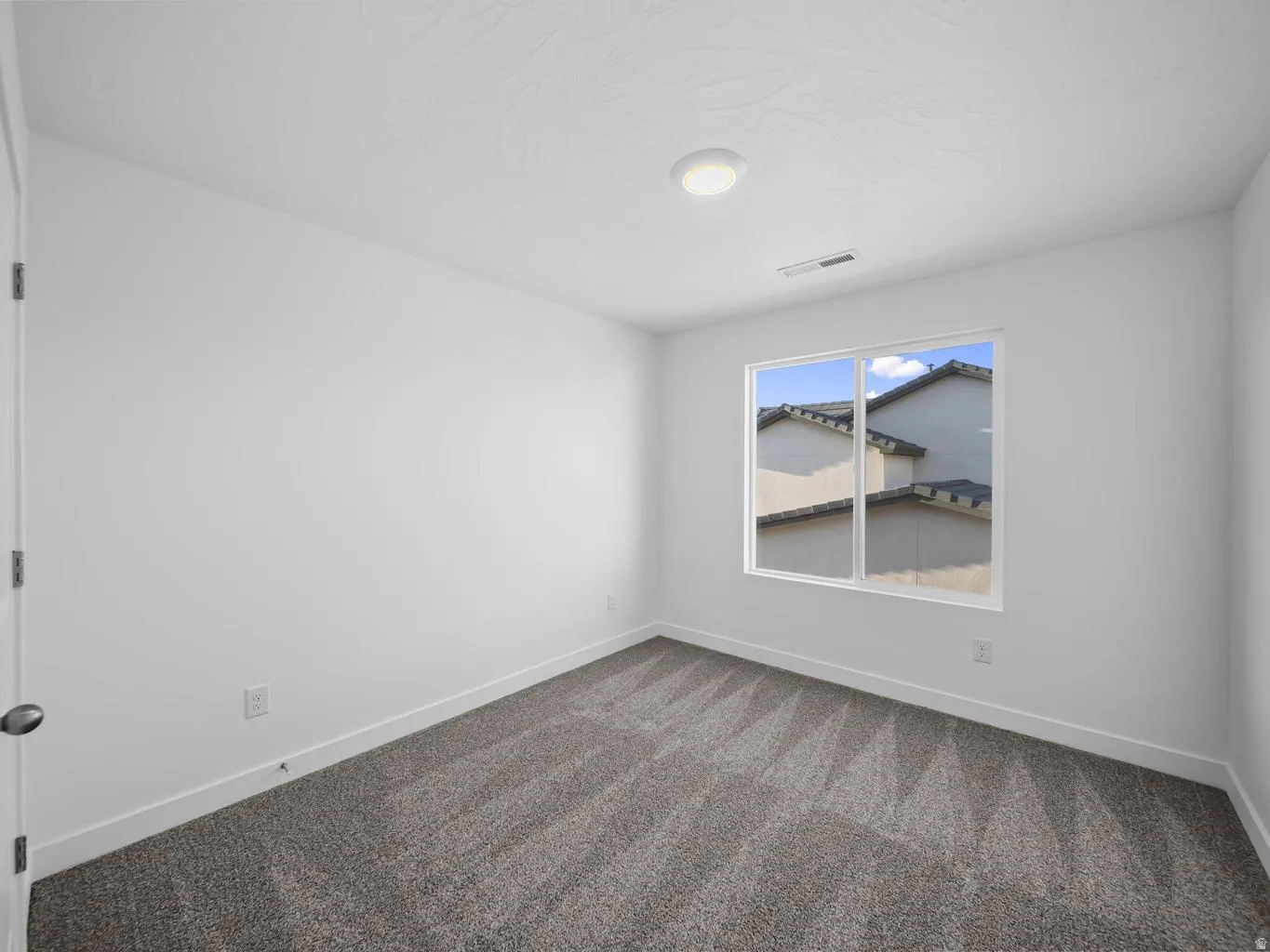 White walls, gray patterned carpet, and a flush-mount ceiling light