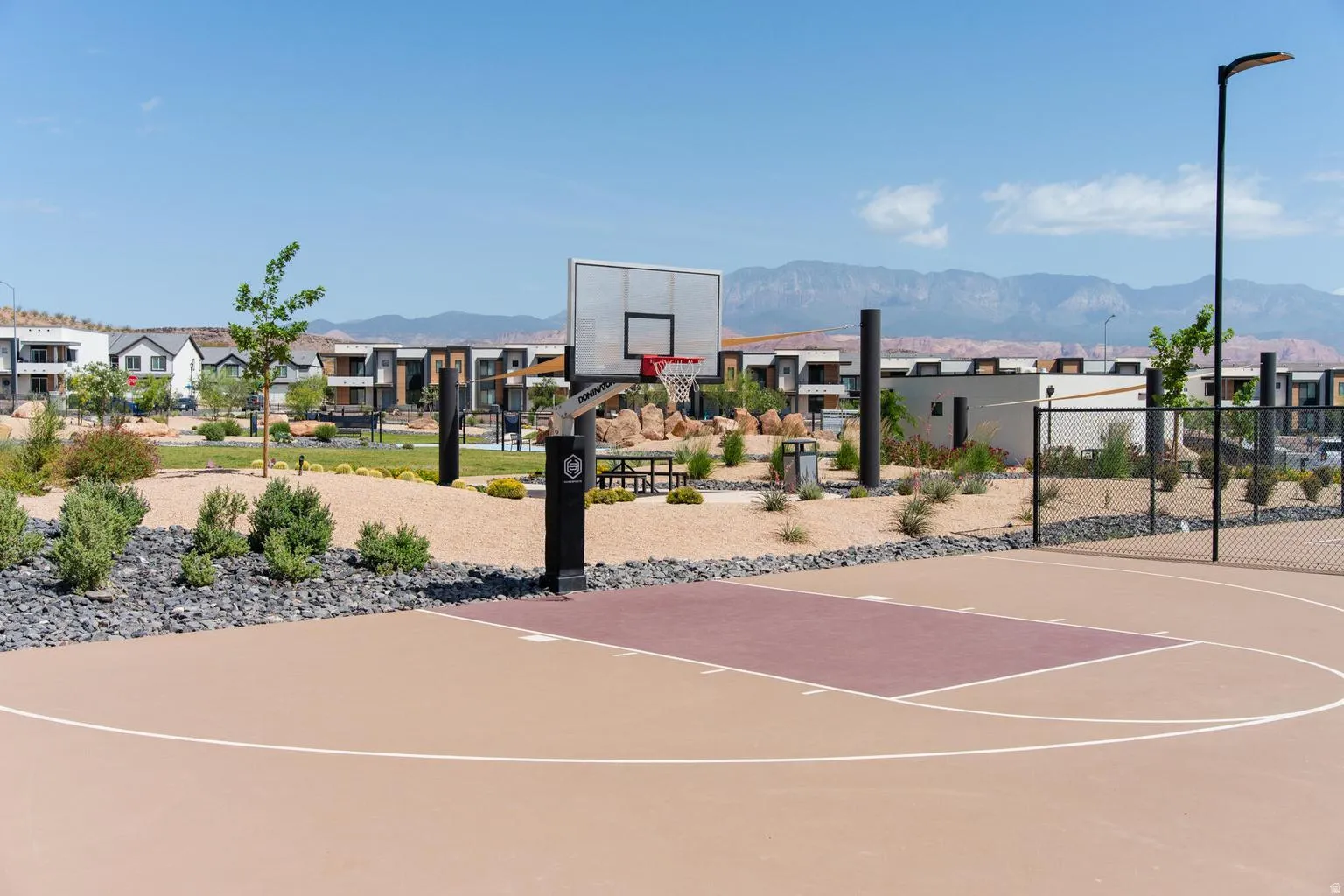 Outdoor basketball court featuring a painted surface, a metal backboard, and a surrounding fence
