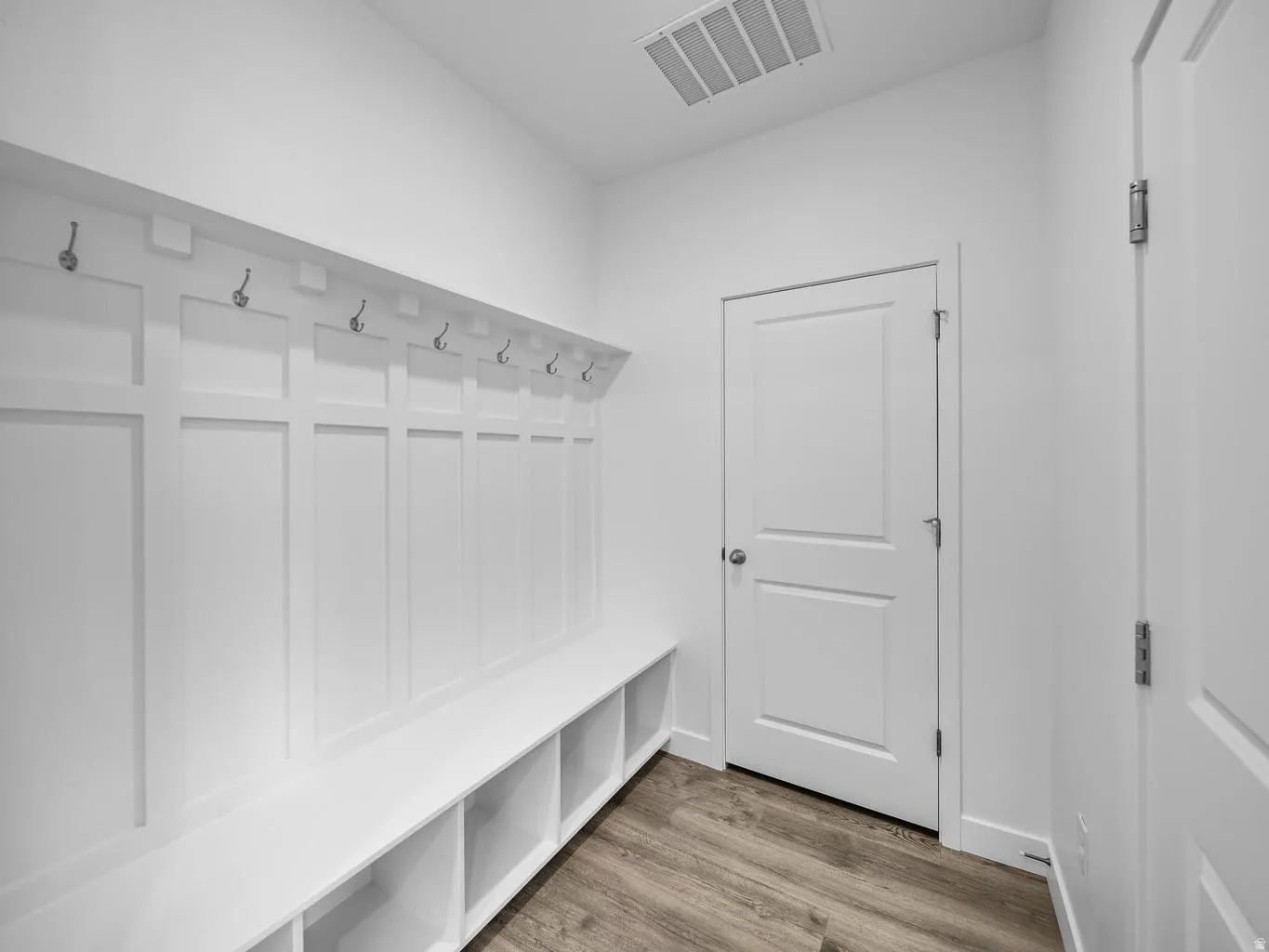 Built-in hall tree with storage cubbies and hooks, wood-finish flooring, and white paneled doors