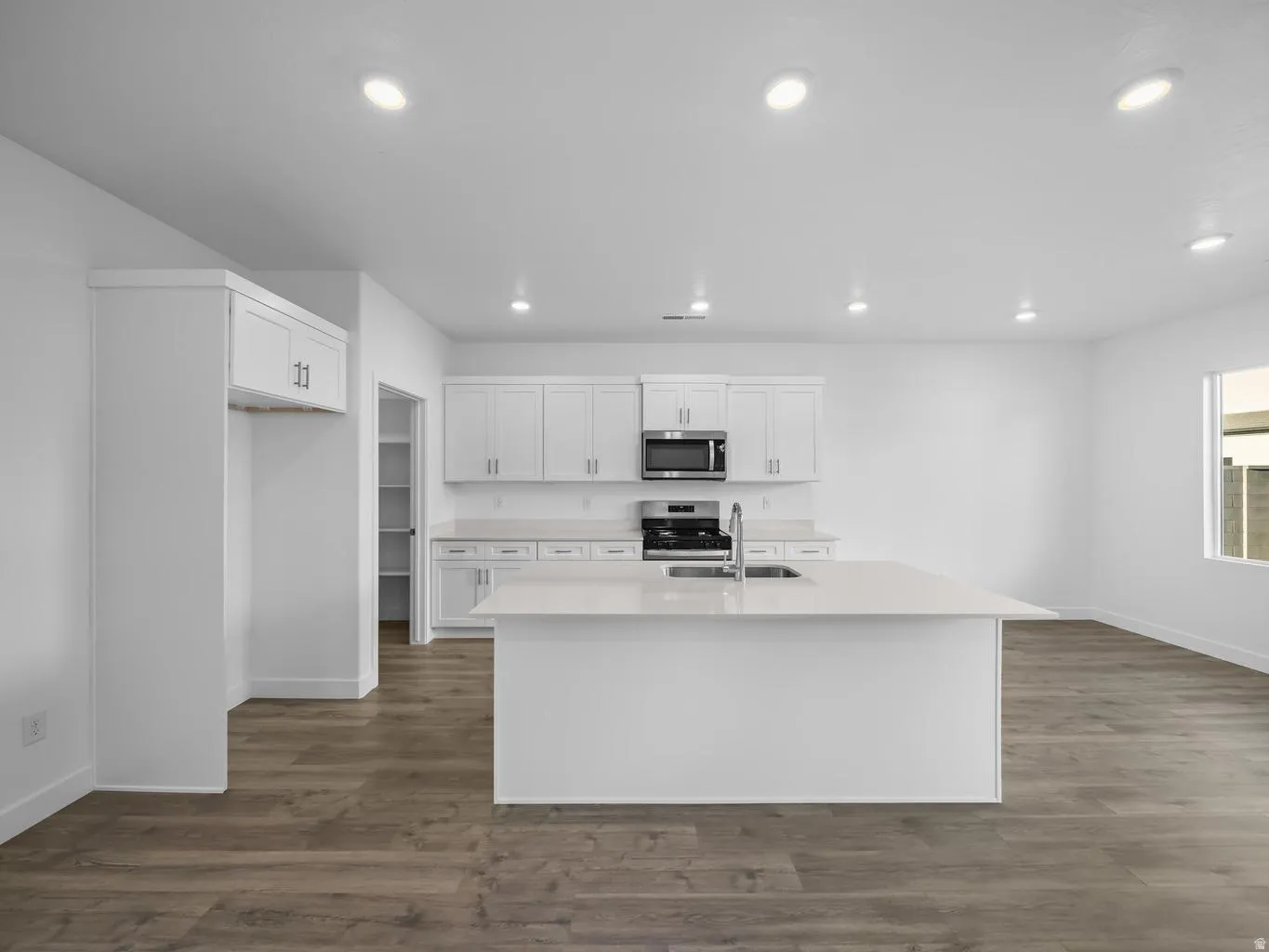 Kitchen featuring wood-finish flooring, white cabinetry, a central island with an integrated sink, stainless steel appliances, and recessed lighting