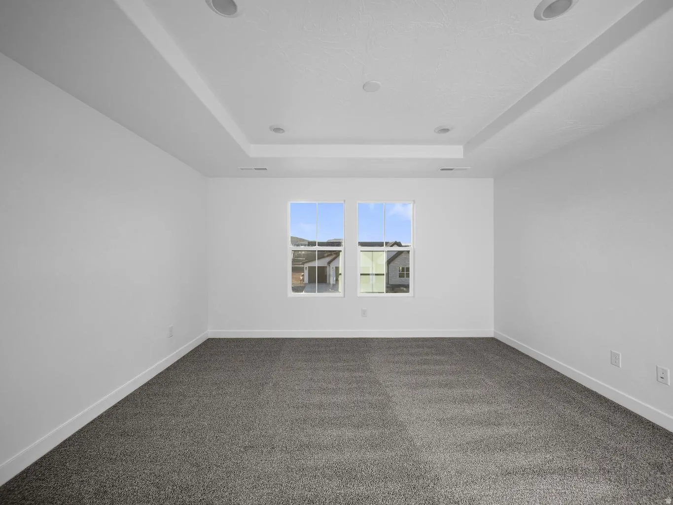 Tray ceiling with recessed lighting, dual windows, plush gray carpeting, and white wall finishes