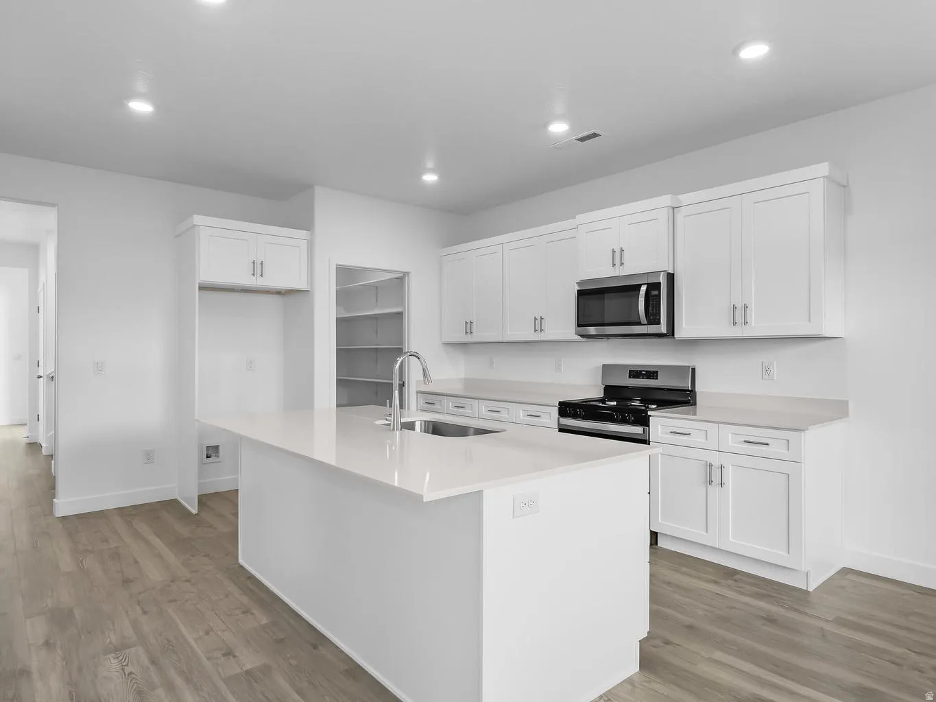 Kitchen featuring white cabinetry, light-toned countertops, a stainless steel microwave, a built-in pantry, and wood-finish flooring