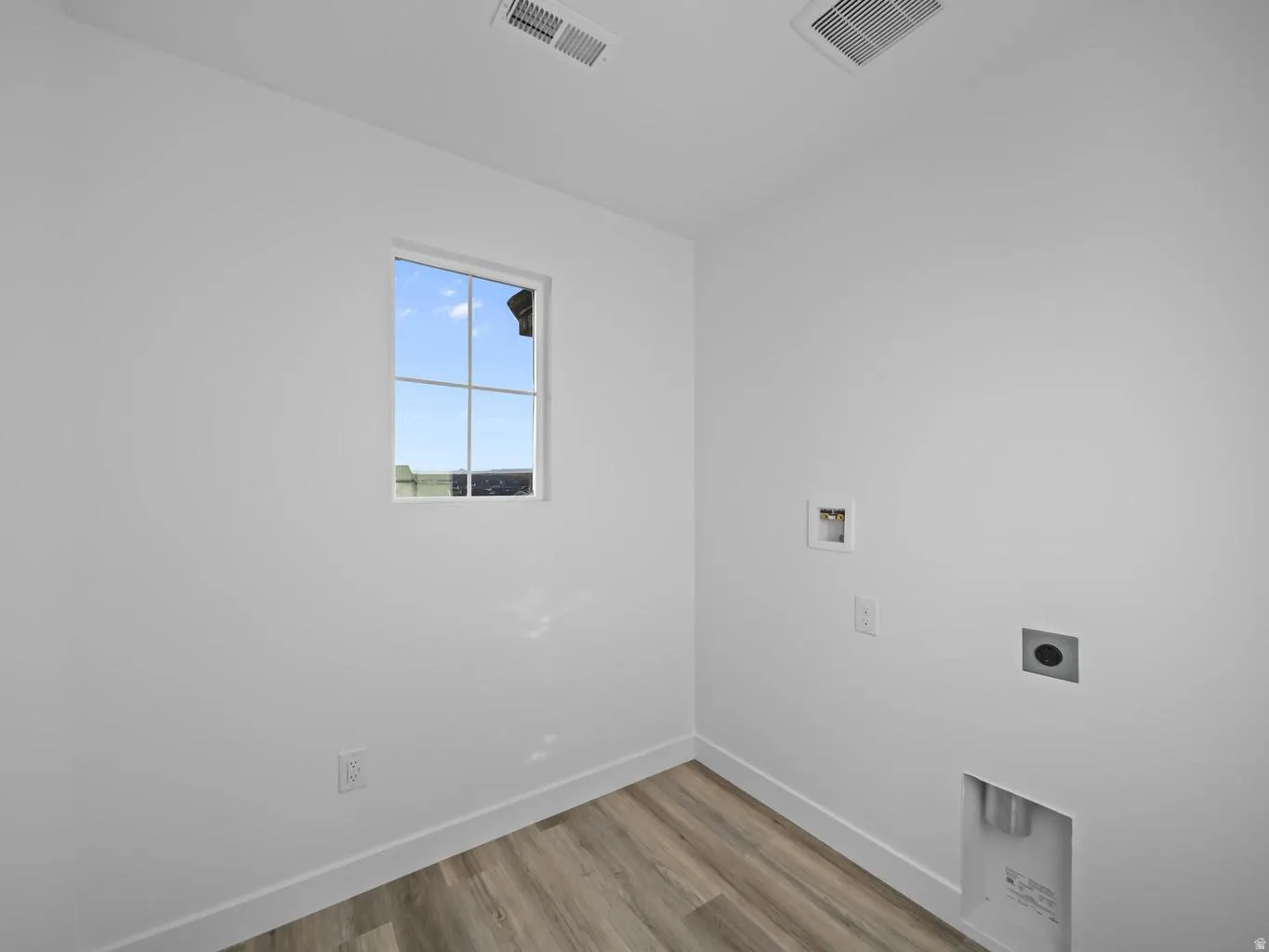 Room featuring a window, white walls, wood-finish flooring, and utility hookups