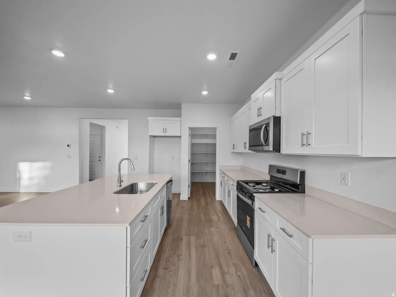 Kitchen featuring white shaker cabinetry, light-toned countertops, stainless steel appliances, and wood-finish flooring