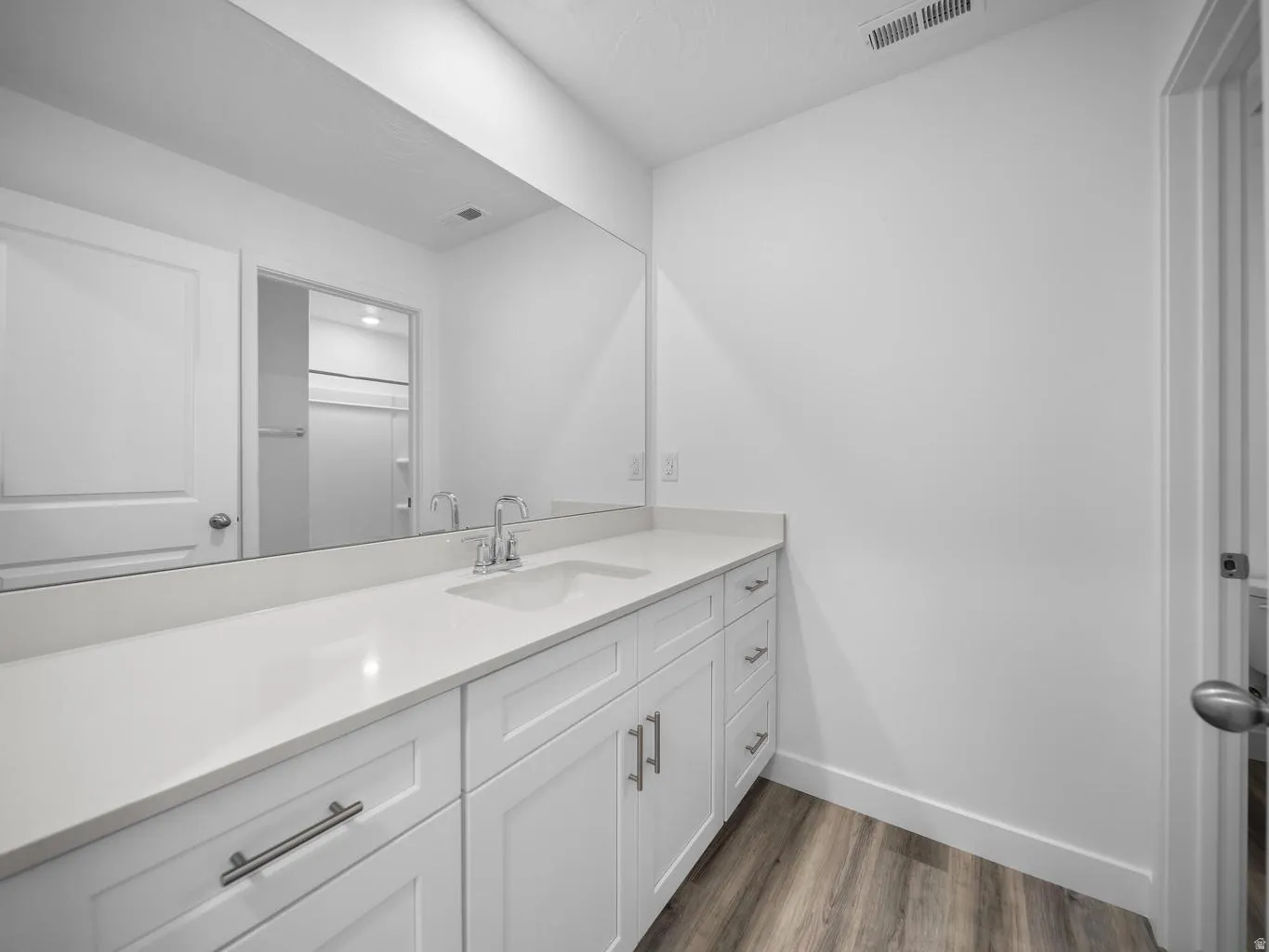 White vanity with silver-tone hardware, an integrated single basin sink, and a large wall-mounted mirror