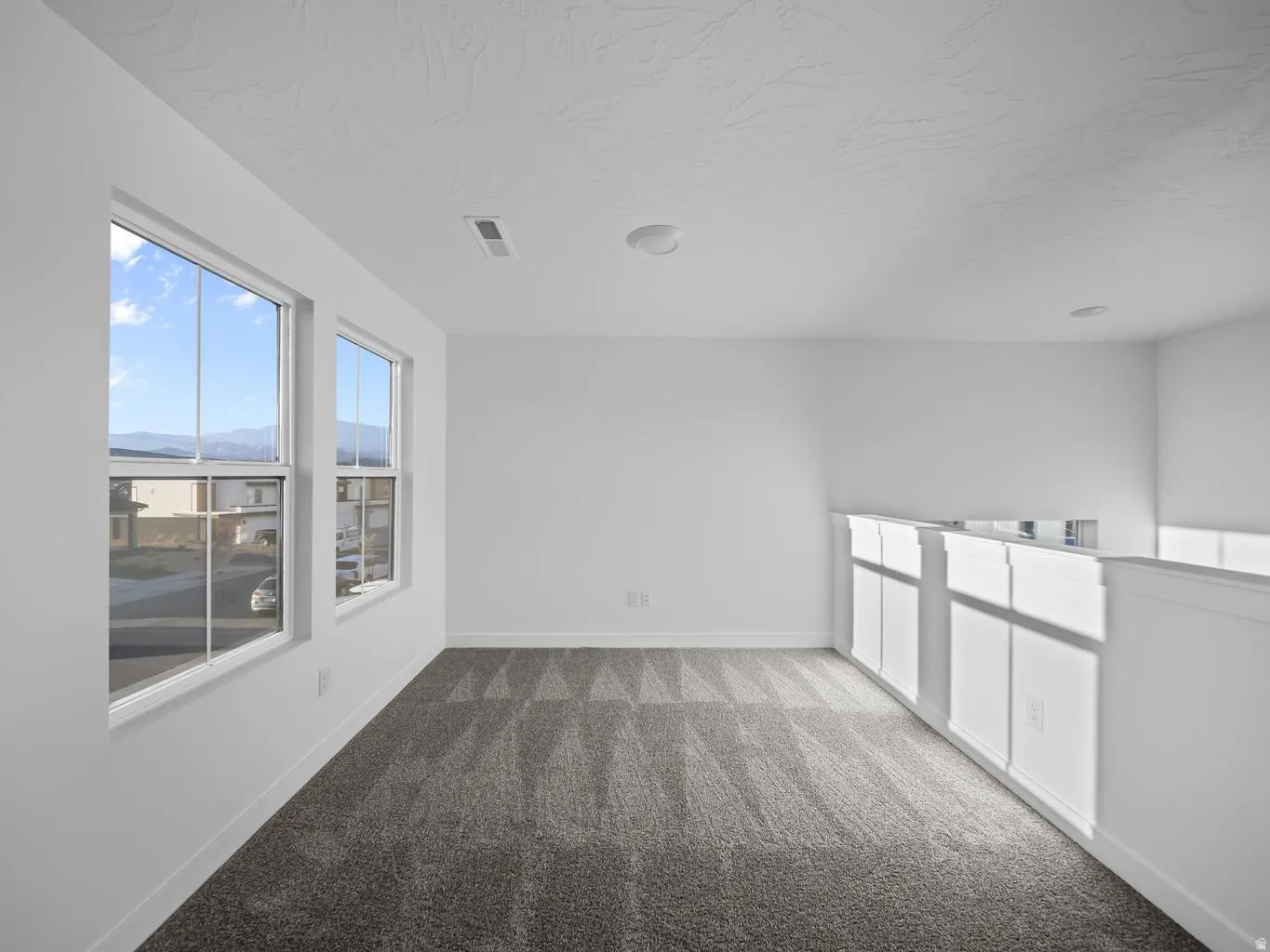 White walls, two large windows, textured carpet, and white railing