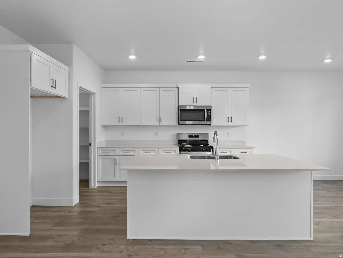 Contemporary kitchen featuring white cabinetry, light-toned countertops, stainless steel appliances, a center island with an undermount sink, and wood-finish flooring