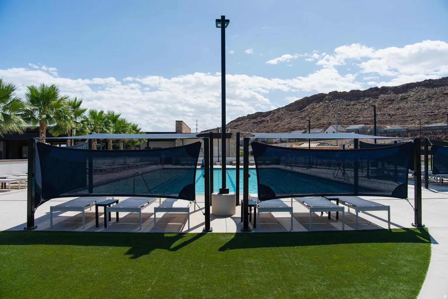 Resort-style pool with integrated shade structures, ample lounge seating, and surrounding synthetic turf