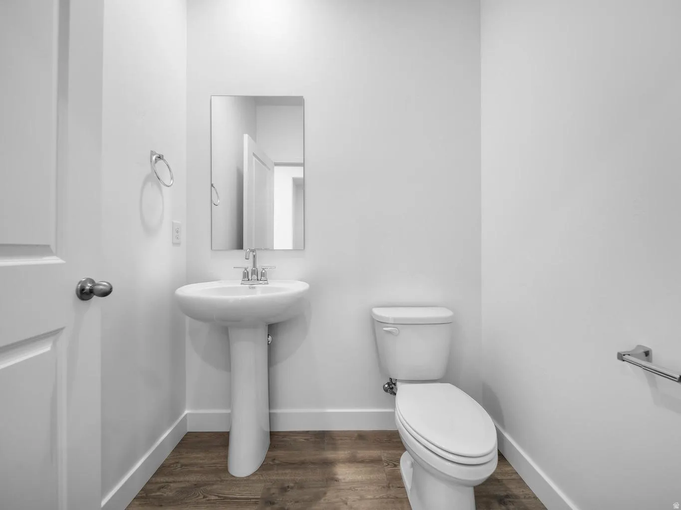 Pedestal sink with chrome faucet, wall-mounted mirror, white toilet, and wood-finish flooring