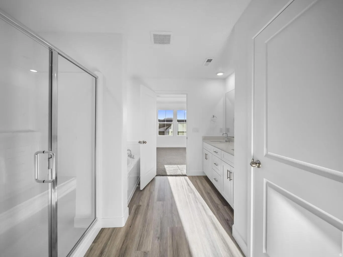 Glass-enclosed shower with bench seating, soaking tub, dual vanity with undermount sinks, and wood-finish flooring