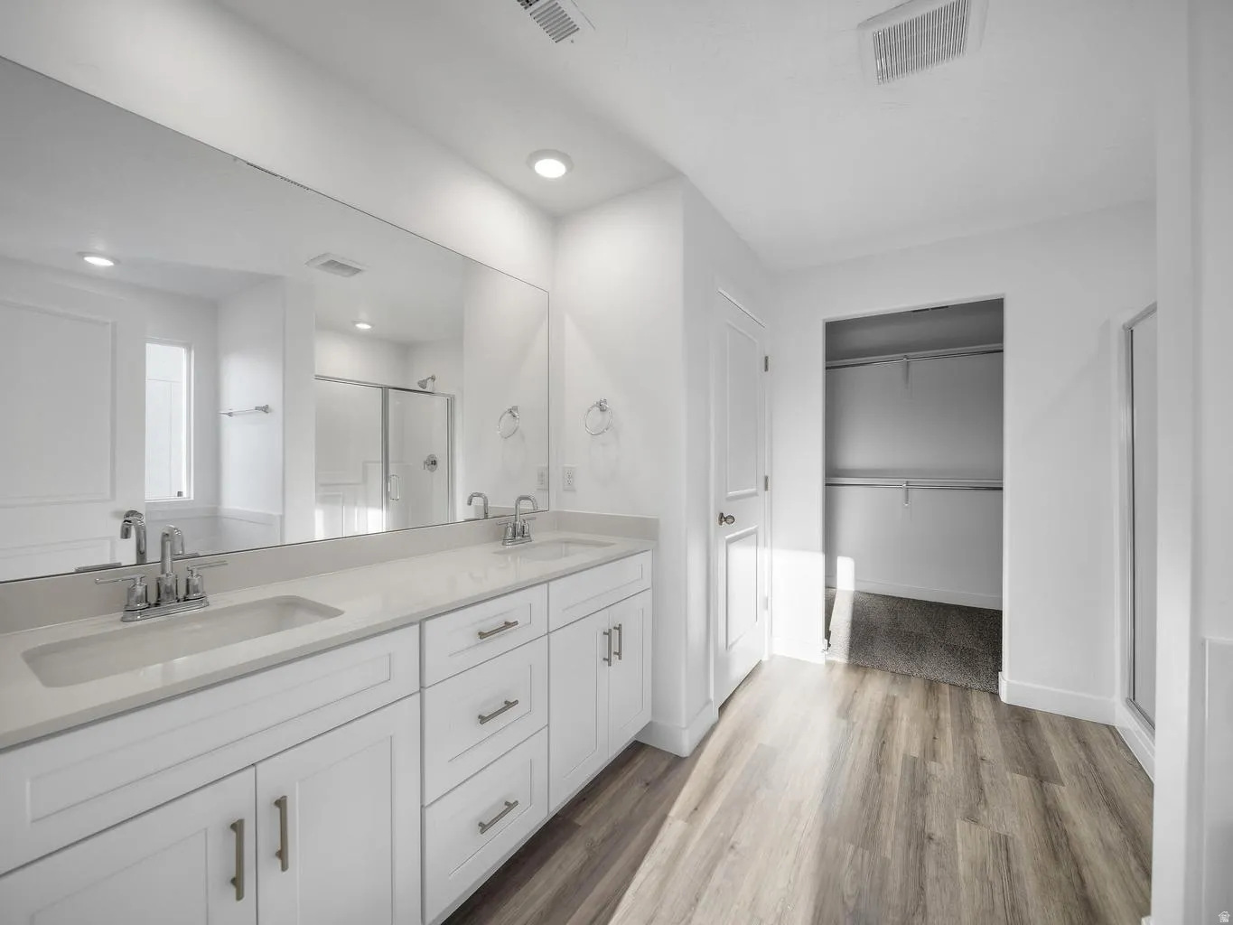 Double vanity with undermount sinks, wood-finish flooring, white cabinetry, and recessed lighting
