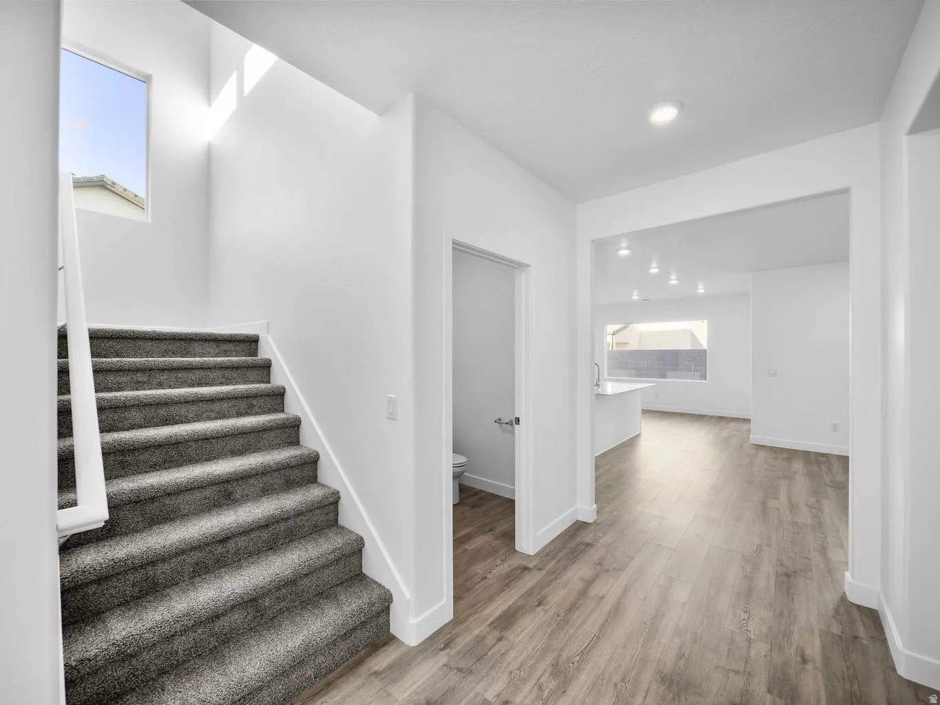 Carpeted staircase with white railing, wood-finish flooring, recessed lighting, and a skylight