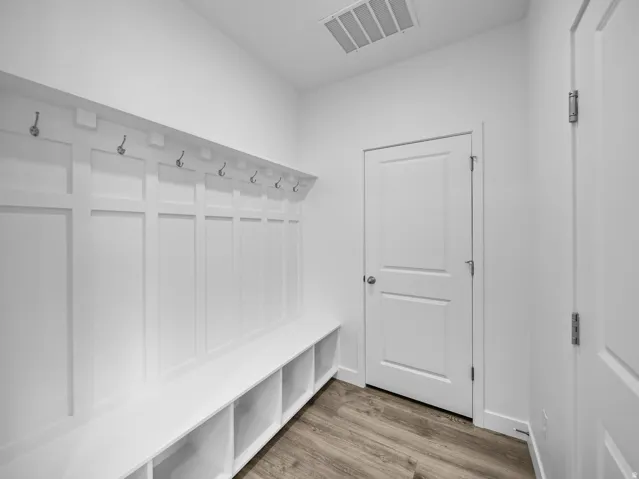 Built-in hall tree with storage cubbies and hooks, wood-finish flooring, and white paneled doors