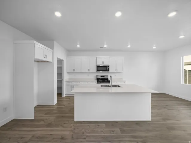 Kitchen featuring wood-finish flooring, white cabinetry, a central island with an integrated sink, stainless steel appliances, and recessed lighting