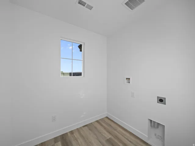 Room featuring a window, white walls, wood-finish flooring, and utility hookups