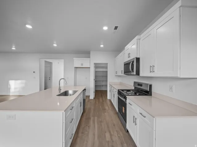 Kitchen featuring white shaker cabinetry, light-toned countertops, stainless steel appliances, and wood-finish flooring