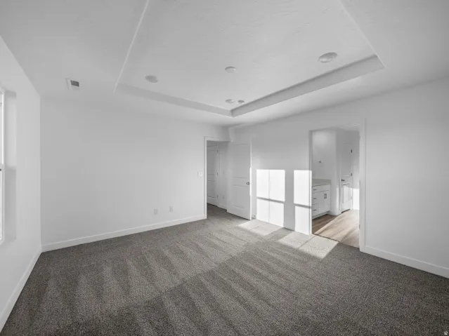 Recessed ceiling lighting, tray ceiling, neutral wall tones, carpeted flooring, and a window