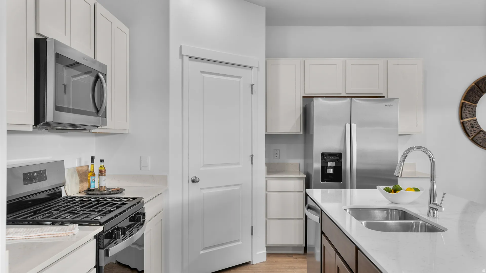 Kitchen featuring white cabinetry, stainless steel appliances, a center island with an undermount sink, and light-toned countertops