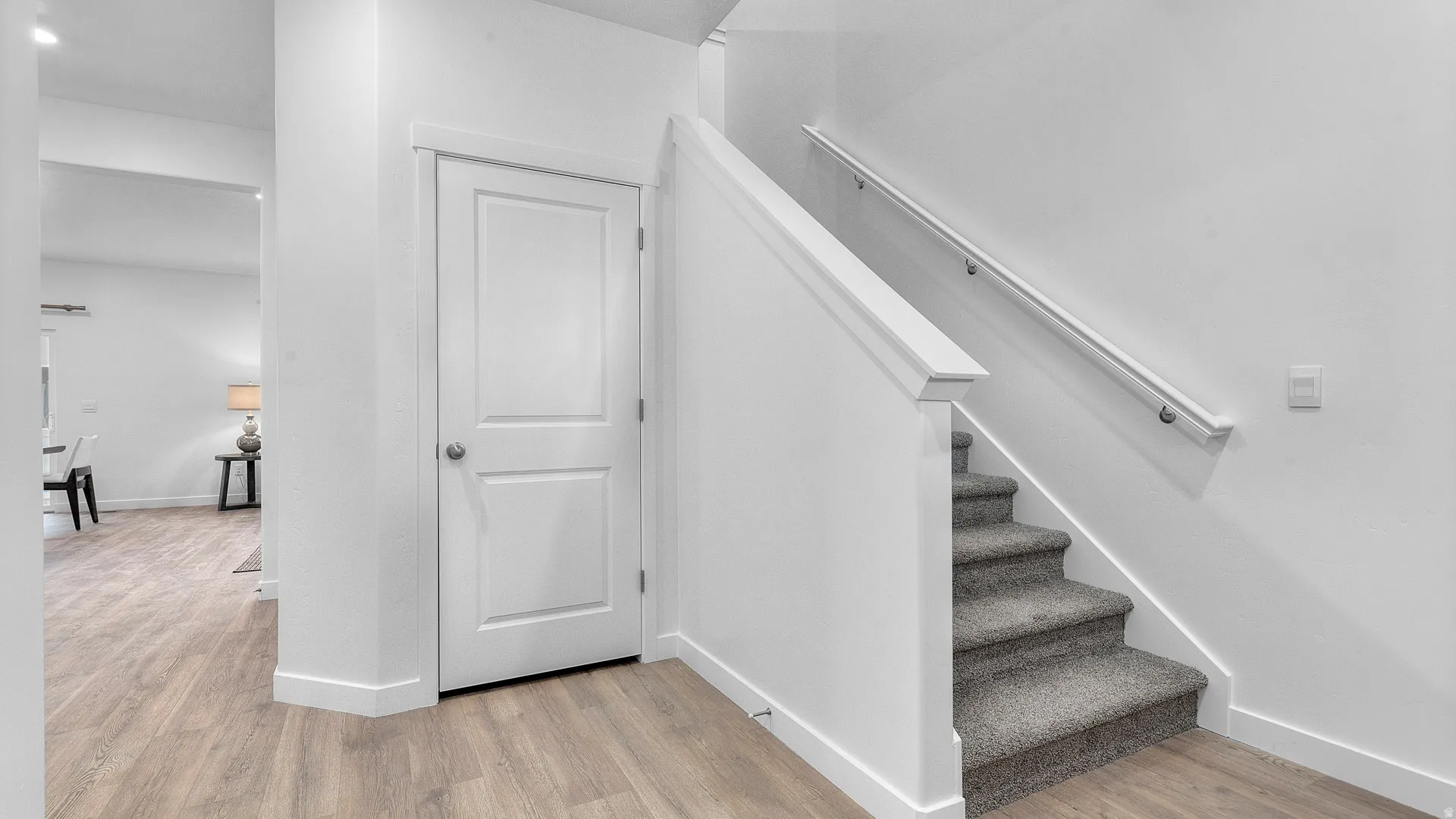 Wood-finish flooring, white paneled door, carpeted staircase, and a white handrail