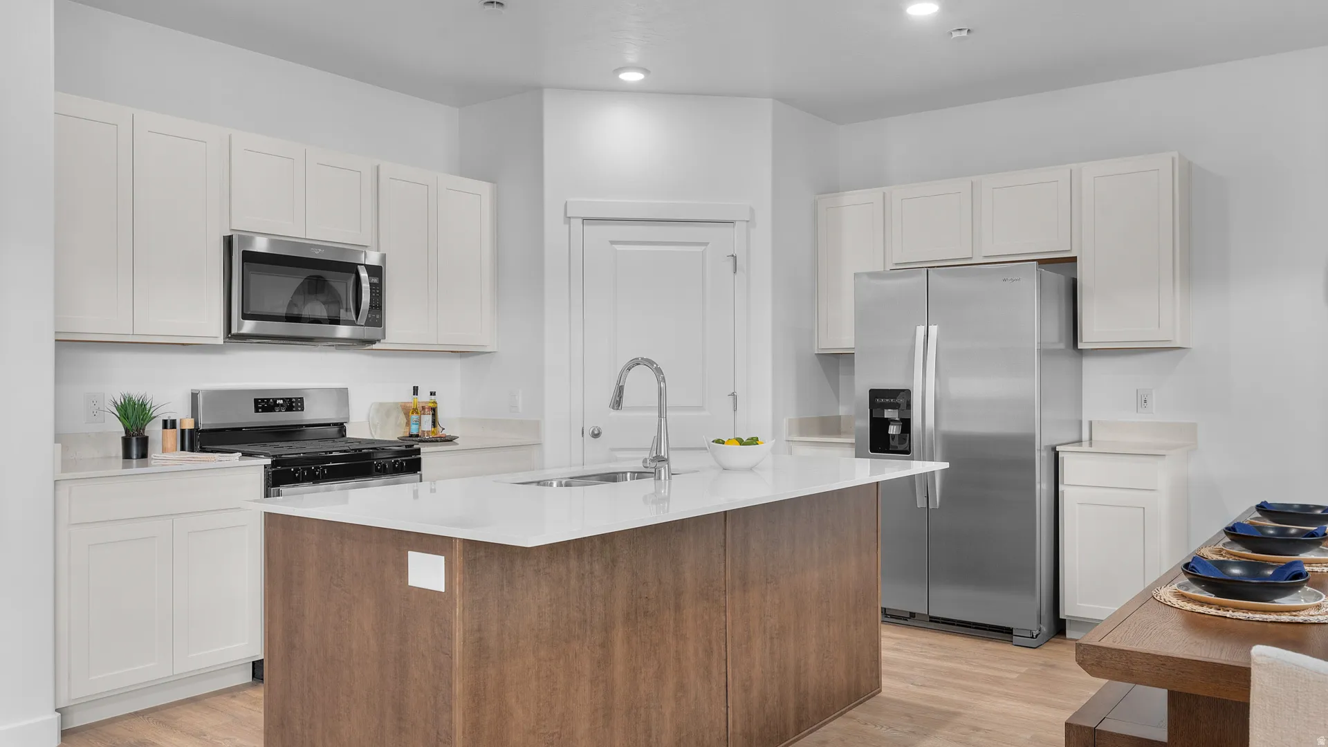 Kitchen featuring white cabinetry, stainless steel appliances, a center island with sink, light countertops, and wood-finish flooring