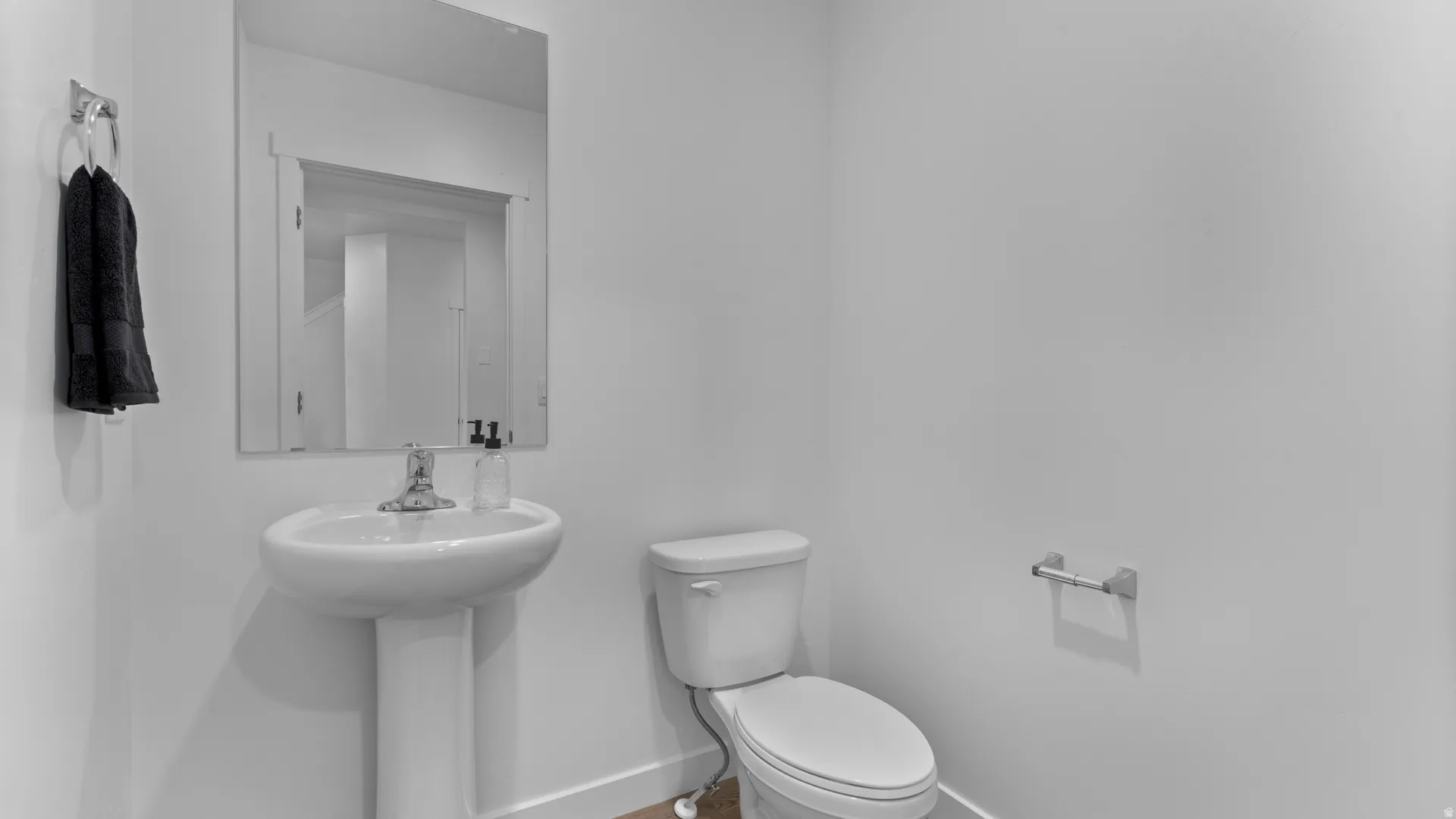 Pedestal sink with chrome faucet, wall-mounted mirror, and white toilet