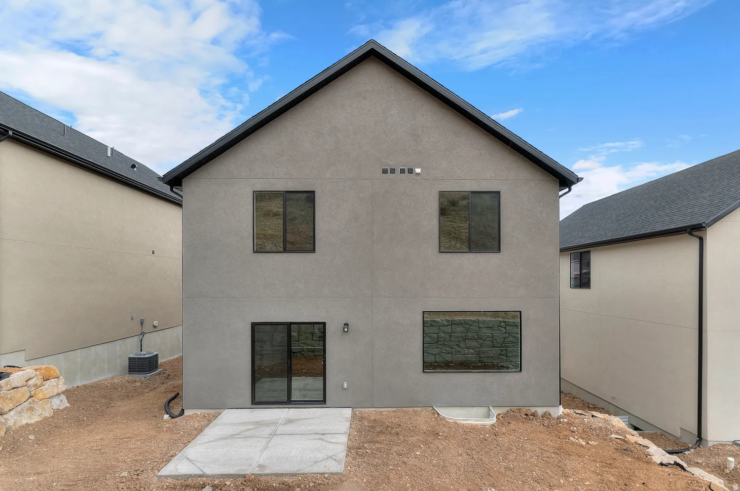 Rear exterior with gray stucco finish, black-framed windows, and a sliding glass door