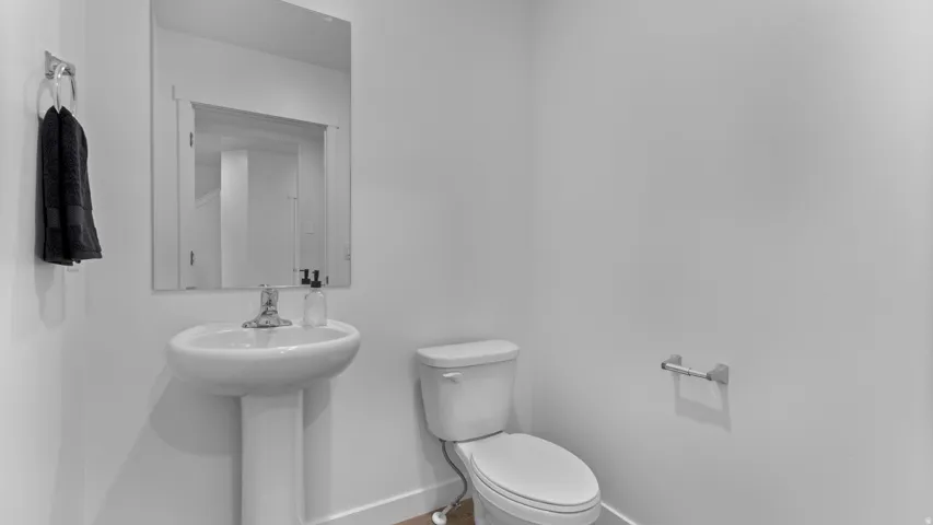 Pedestal sink with chrome faucet, wall-mounted mirror, and white toilet