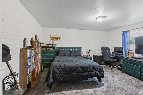 White painted brick wall, light-colored walls, window with natural light, textured ceiling, and a flush-mount light fixture