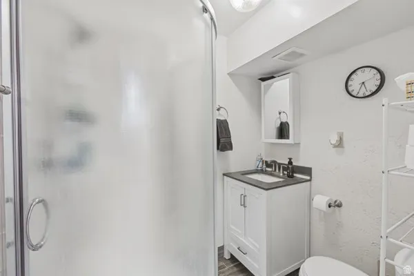 Frosted glass shower enclosure, single vanity with dark countertop, white shaker-style cabinetry, and wall-mounted medicine cabinet
