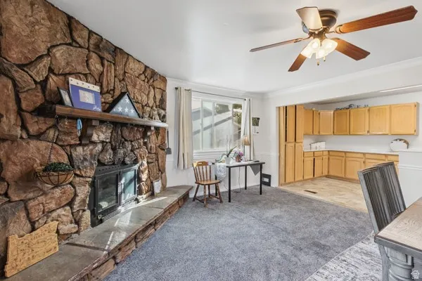Stone-clad fireplace with a wood mantel, ceiling fan with integrated lighting, and wood-finish cabinetry