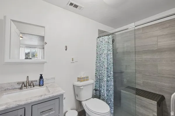 Bathroom featuring a gray vanity with an integrated sink, framed medicine cabinet, glass-enclosed shower, and tiled shower walls