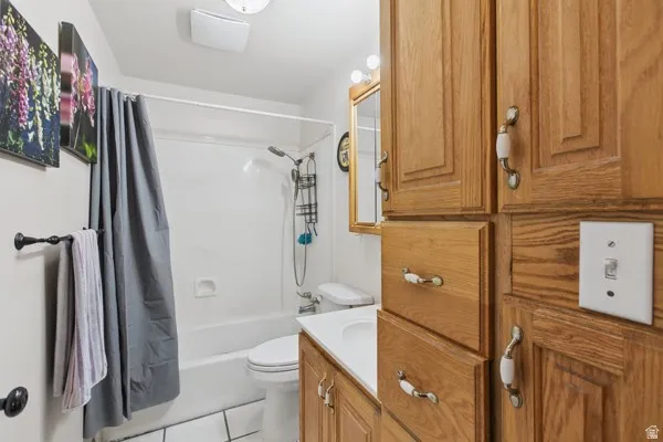 White tile flooring, integrated shower/tub, light wood-finish cabinetry, built-in vanity, and overhead lighting