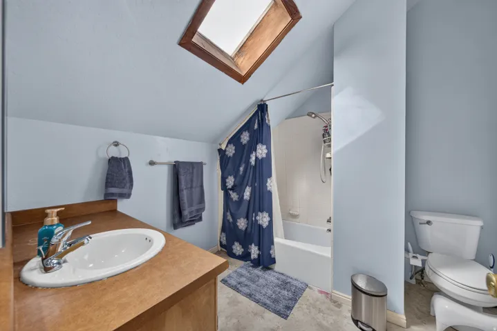 Bathroom featuring a wood-framed skylight, built-in bathtub with shower, and an oval sink with a chrome faucet