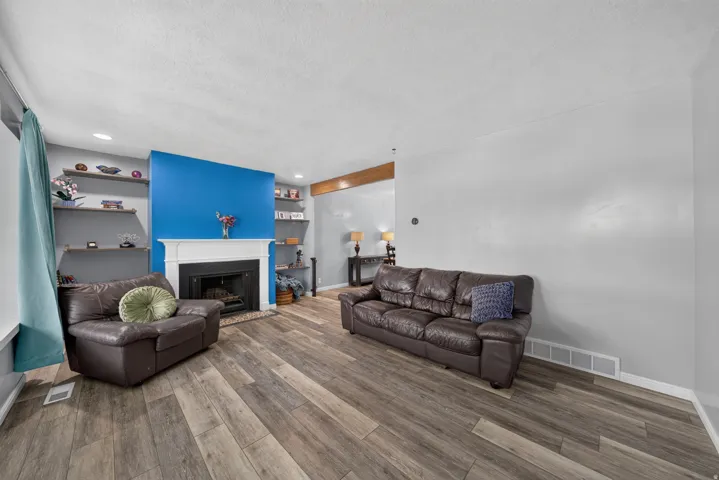 Wood-finish flooring throughout, white mantel fireplace, accent wall, and built-in shelving