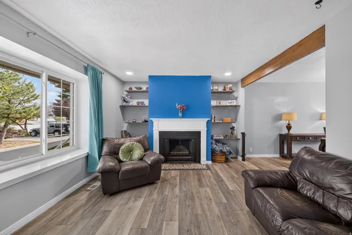 Wood-finish flooring throughout, featuring a fireplace with a white mantel and hearth, built-in shelving, and a prominent wood beam