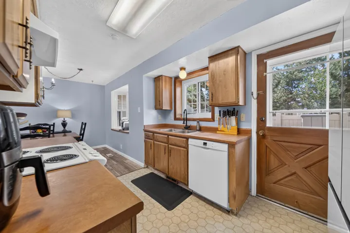 Kitchen featuring wood-finish cabinetry, solid surface countertops, a stainless steel sink with a matte black faucet, and a white dishwasher