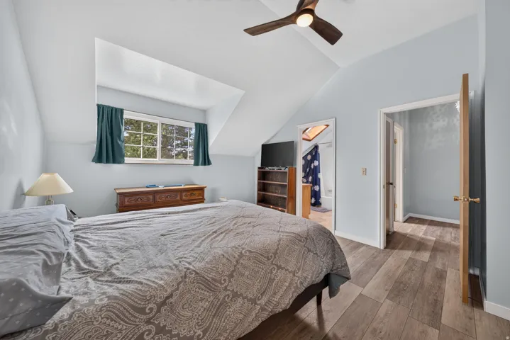 Vaulted ceiling with a ceiling fan, wall-mounted window, wood-finish flooring, and light blue walls