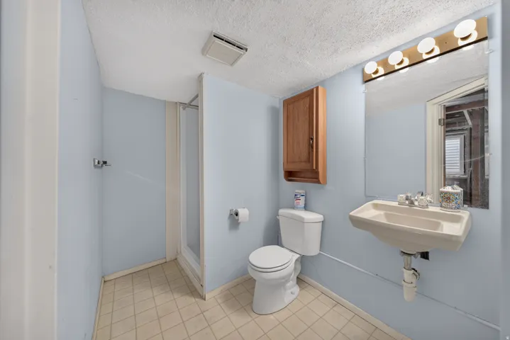 Pedestal sink with chrome fixtures, wood-finish wall cabinet, toilet, and a stand-up shower with frosted glass enclosure