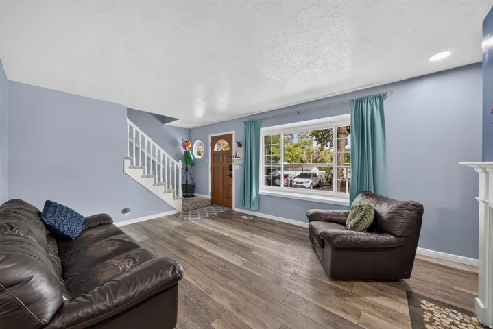 Wood-finish flooring throughout, bright window with natural light, white staircase with balusters, recessed ceiling lighting, and a front entry door with glass inserts