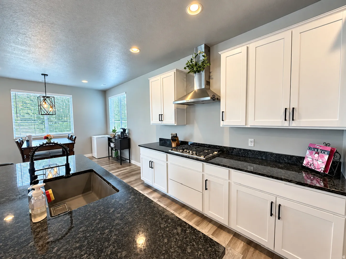 Kitchen featuring dark stone countertops, white shaker cabinetry with black hardware, and wood-finish flooring