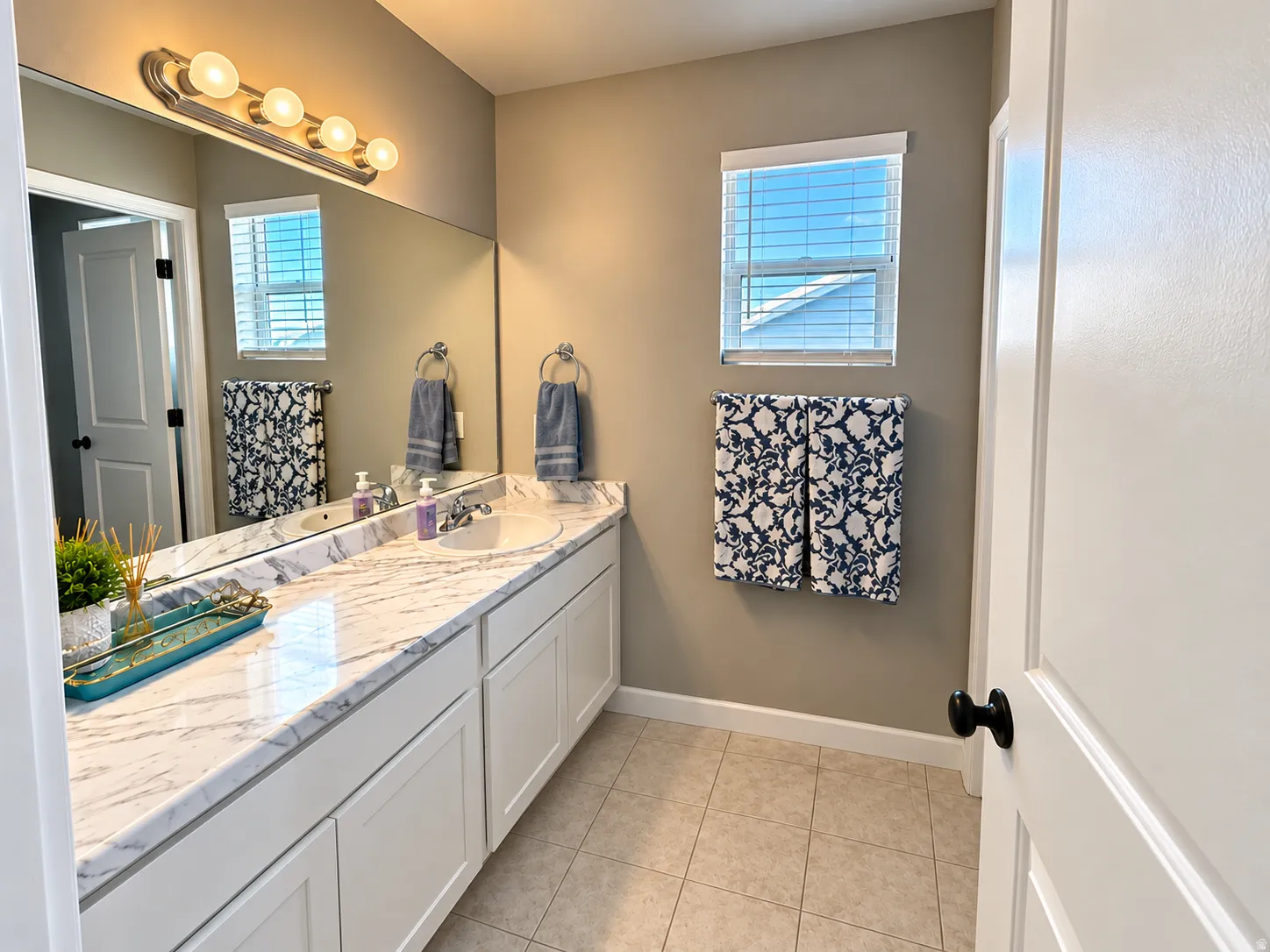 Spacious vanity with a white countertop and integrated sink, dual-door white cabinetry, extended mirror, and a window with blinds