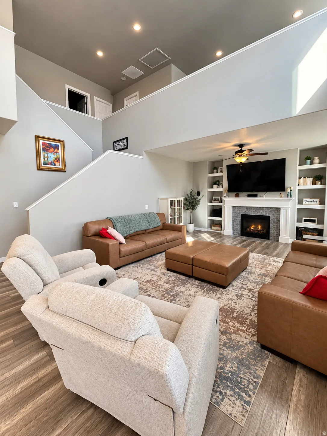 Two-story living area featuring a fireplace with a textured surround, built-in shelving, wood-finish flooring, and recessed lighting
