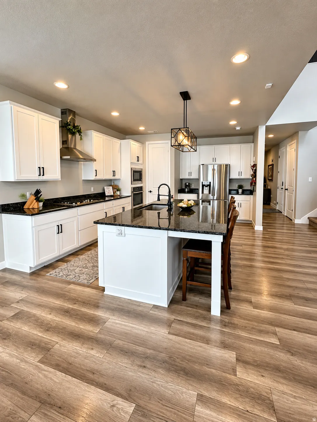 Gourmet kitchen featuring white cabinetry, dark stone countertops, stainless steel appliances, a center island with sink, and wood-finish flooring