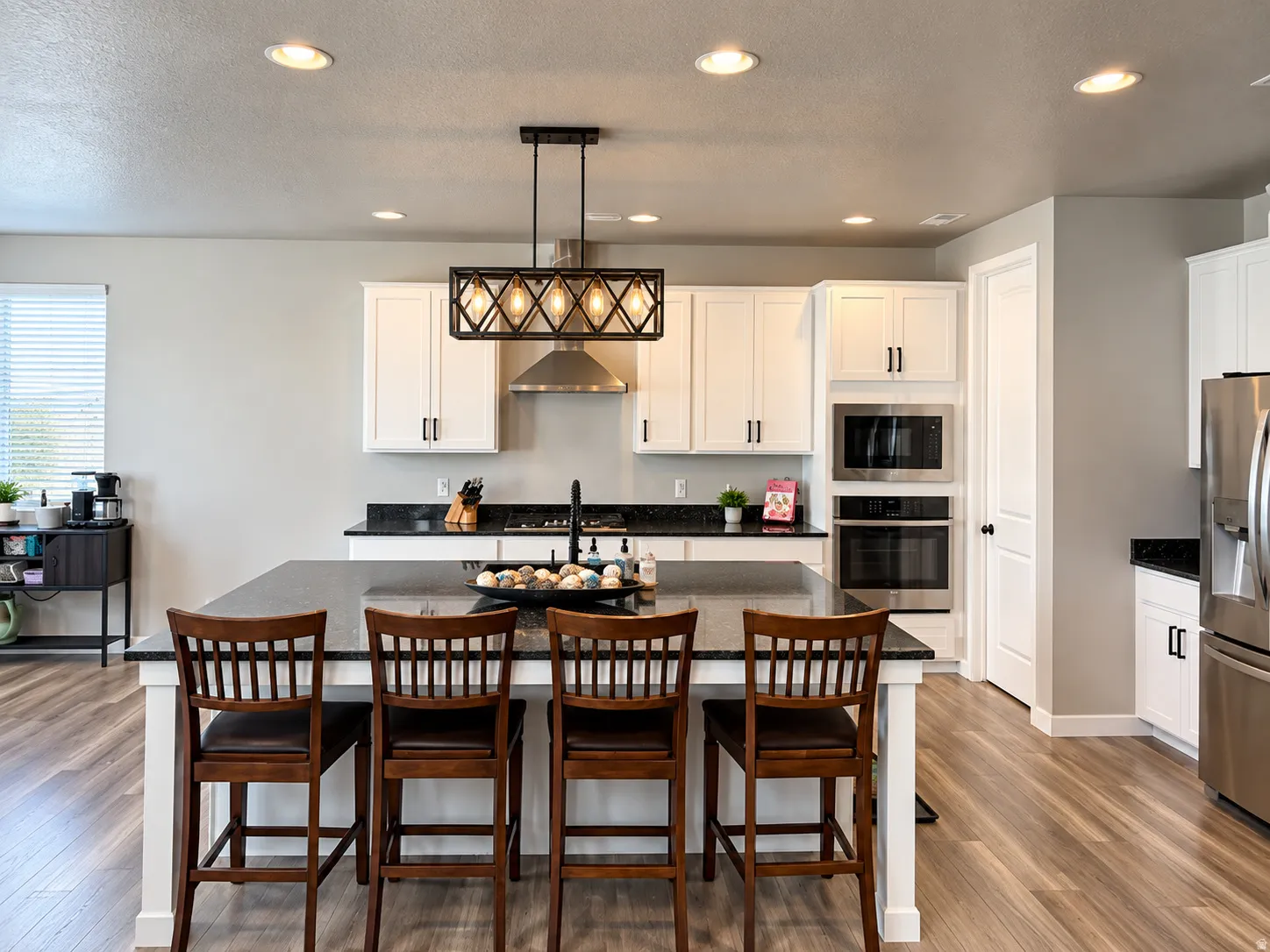 Kitchen featuring a large island with seating, dark countertops, white cabinetry, stainless steel appliances, and wood-finish flooring