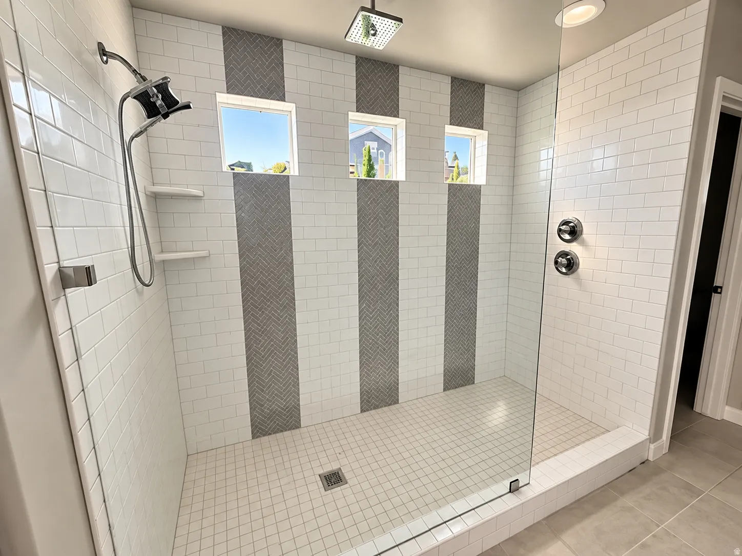 Walk-in shower featuring white subway tile, vertical gray herringbone accent tile, and a glass enclosure