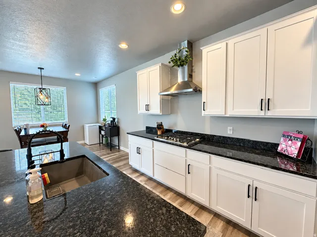 Kitchen featuring dark stone countertops, white shaker cabinetry with black hardware, and wood-finish flooring