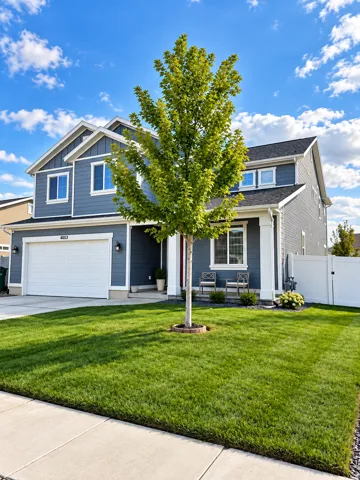 Two-story residence featuring blue siding, white trim accents, a two-car garage, and a lush lawn