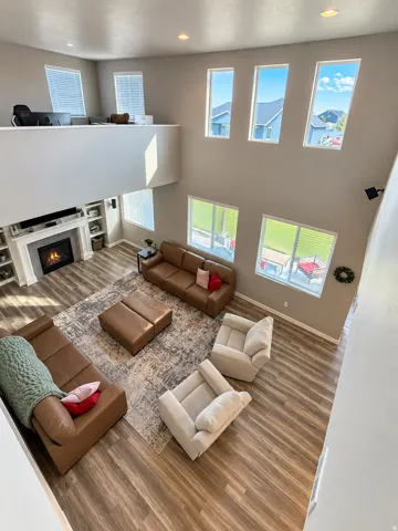 Vaulted ceiling living area featuring multiple windows, recessed lighting, a fireplace with a mantel, and wood-finish flooring