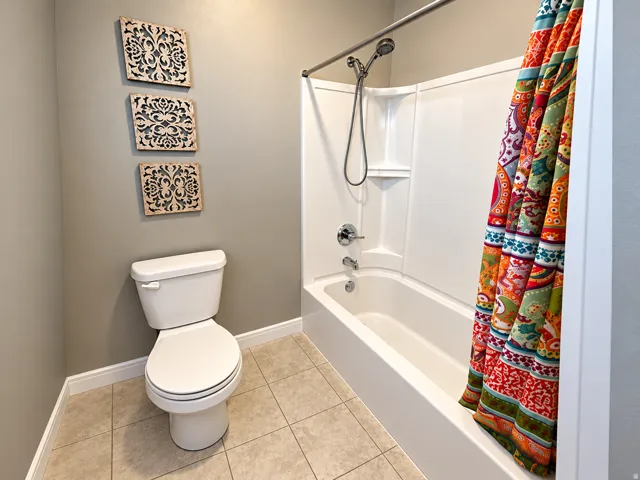 White toilet with a matching tank, a built-in shower/tub combination, and tiled flooring