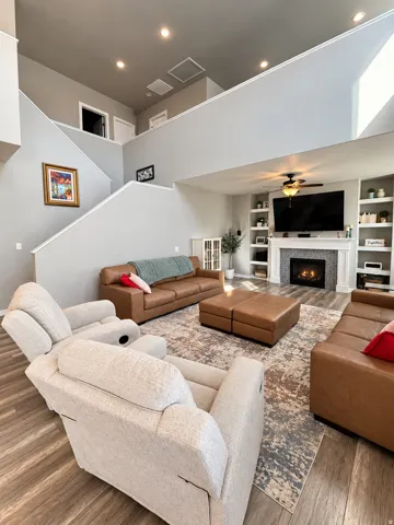 Two-story living area featuring a fireplace with a textured surround, built-in shelving, wood-finish flooring, and recessed lighting